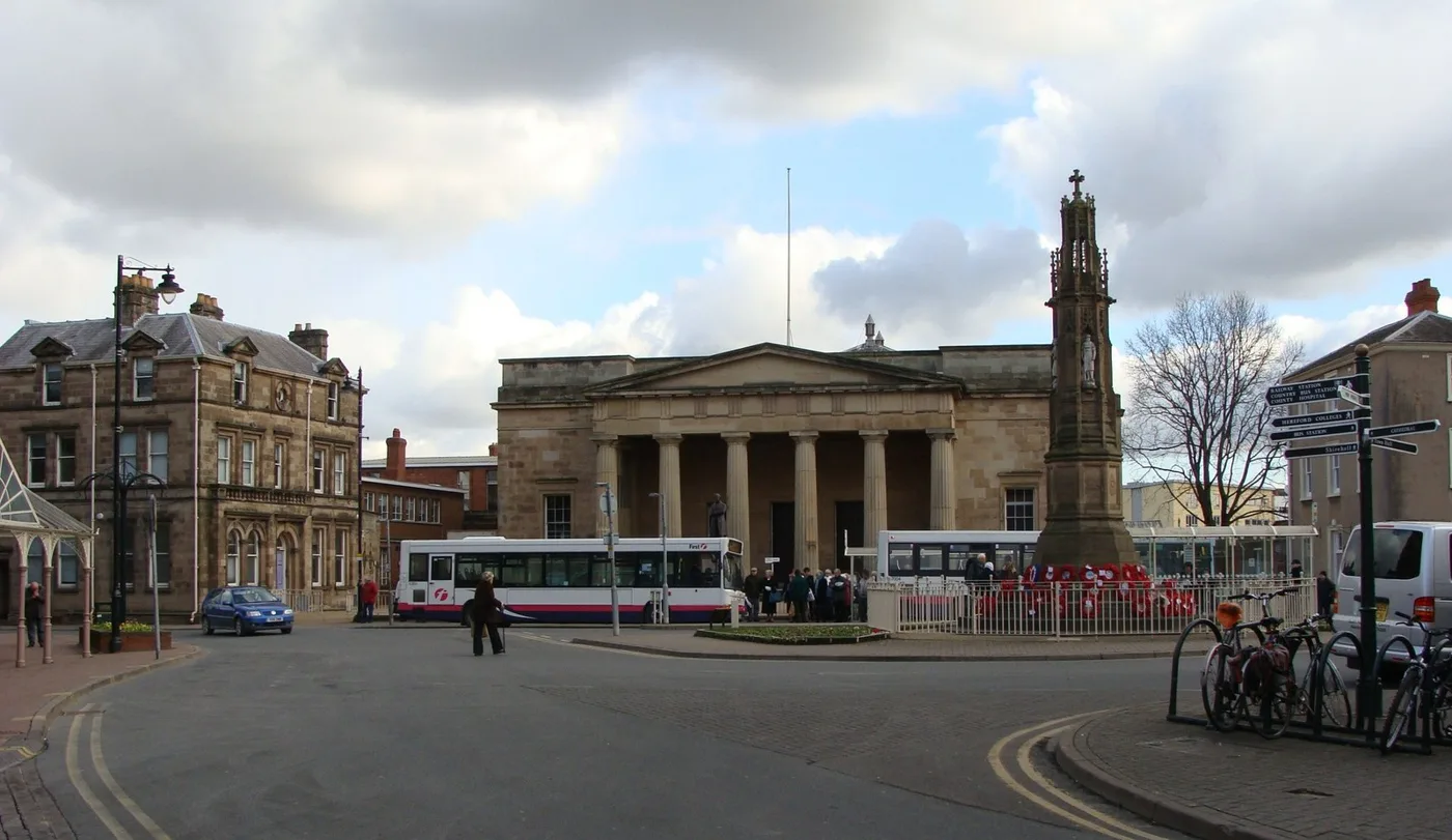 The war memorial in St Peter's Square, Hereford, with wreaths laid at its base and Shire Hall behind